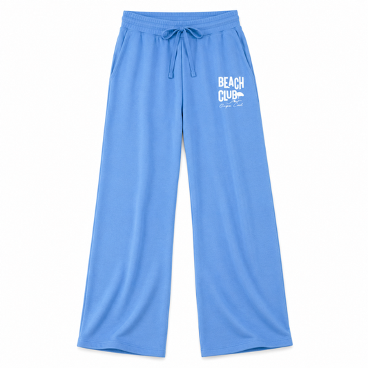Light blue wide-leg lounge pants with a white 'BEACH CLUB' graphic on the left thigh, featuring an elastic drawstring waistband, photographed on a solid white background.