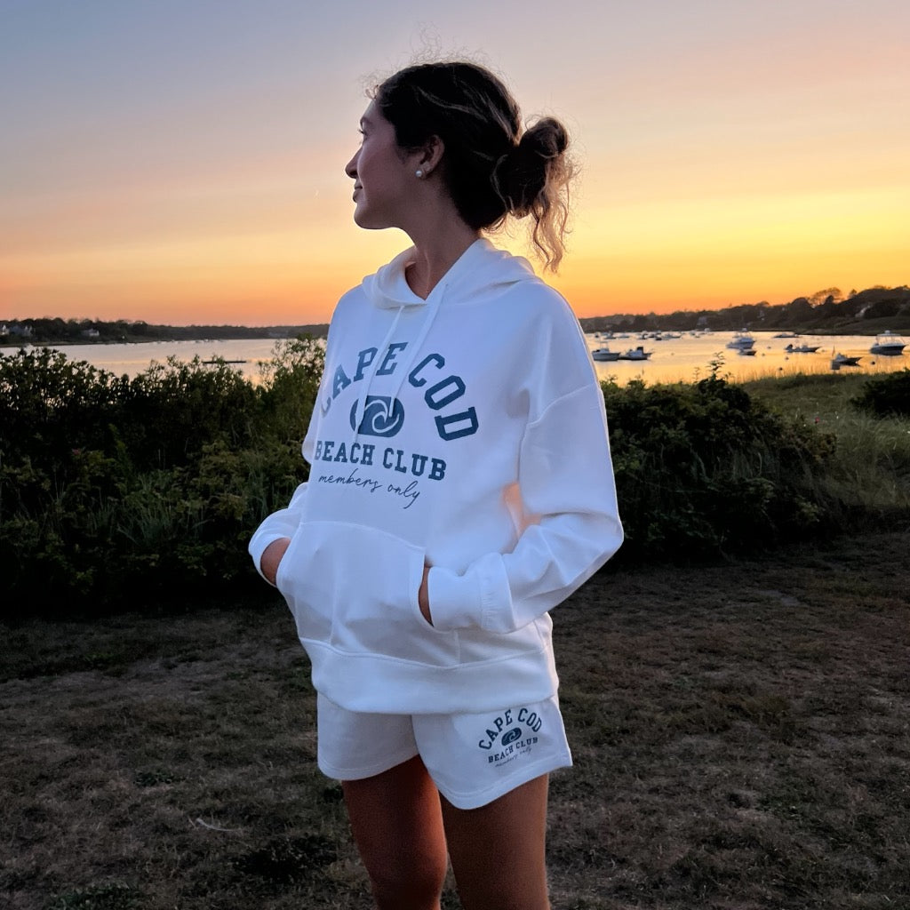 Young woman wearing a cloud, fleece Cape Cod, beach club sweatshirt, and short shorts