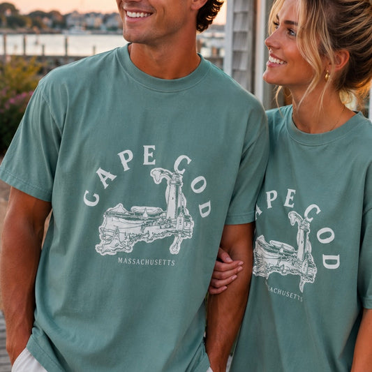 A man and a woman wearing matching green t-shirts with a white graphic of Cape Cod, Massachusetts, in an outdoor setting.